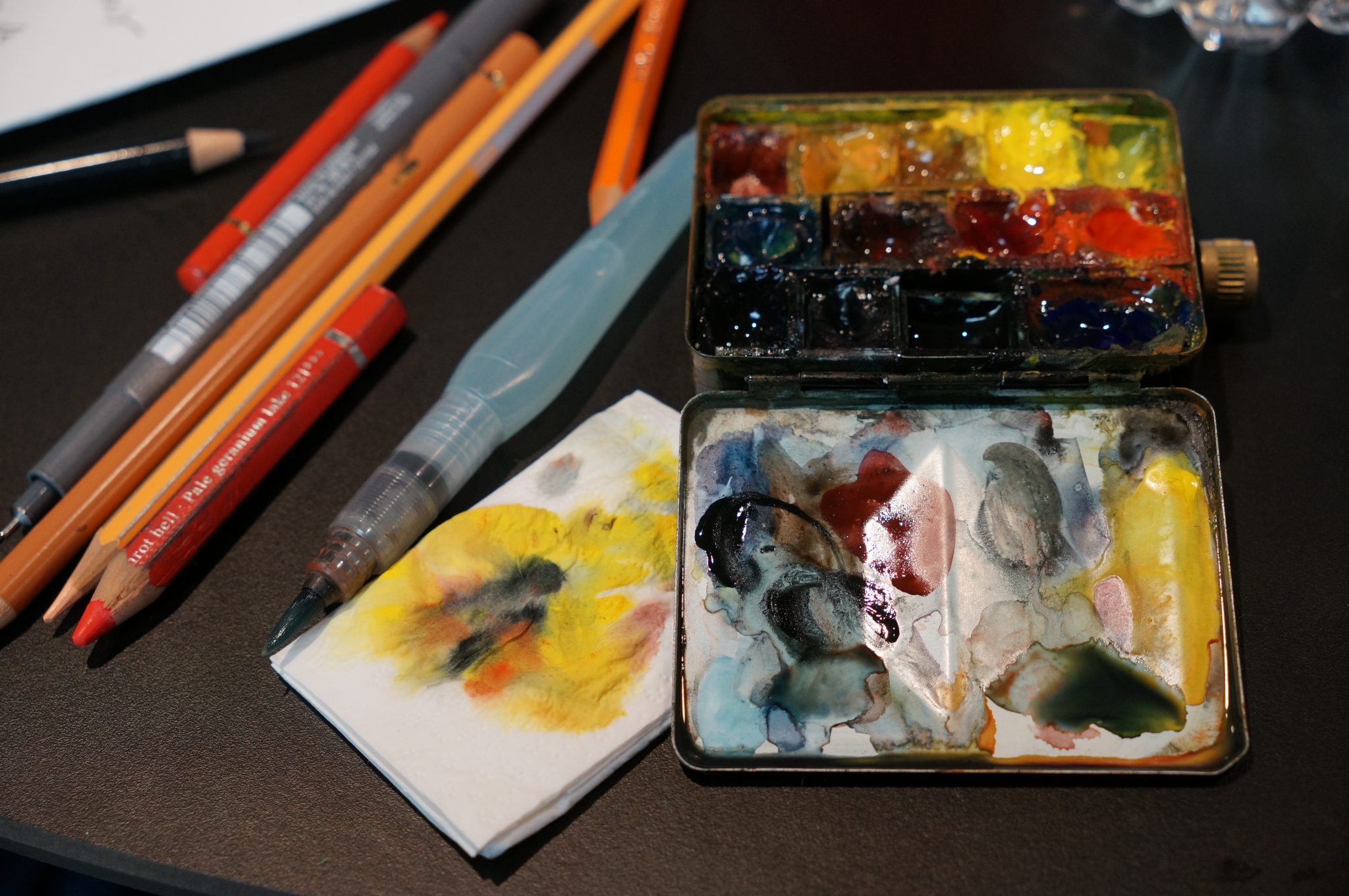 Watercolor palette and color pencils arranged on a creative work surface.
